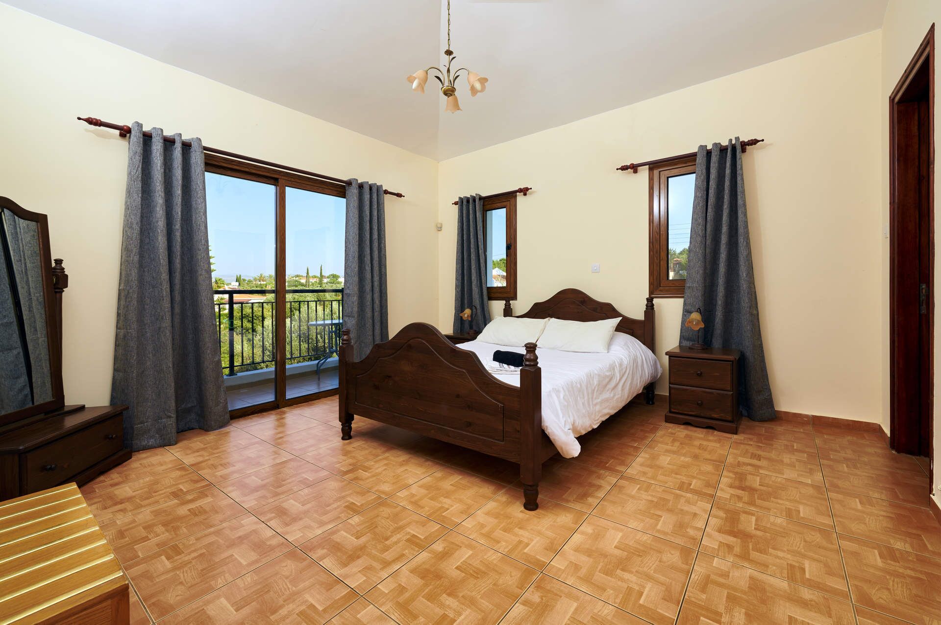 A bedroom with a wooden bed, a nightstand, a dresser, and a balcony with a view.