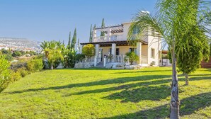 Una casa de dos pisos con balcón, rodeada por un césped cuidado y diversos árboles.