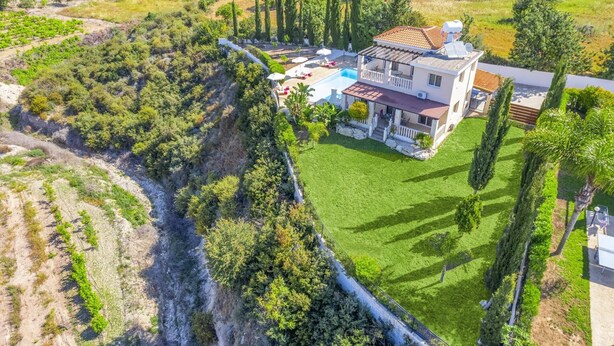 Una casa grande con piscina, rodeada de exuberante vegetación y un acantilado empinado.