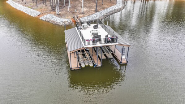 A floating dock with a covered seating area, a small table, and a railing. - Paradise Point on Lake Lanier - large home w/ private dock, games, private cove  (Gainesville)