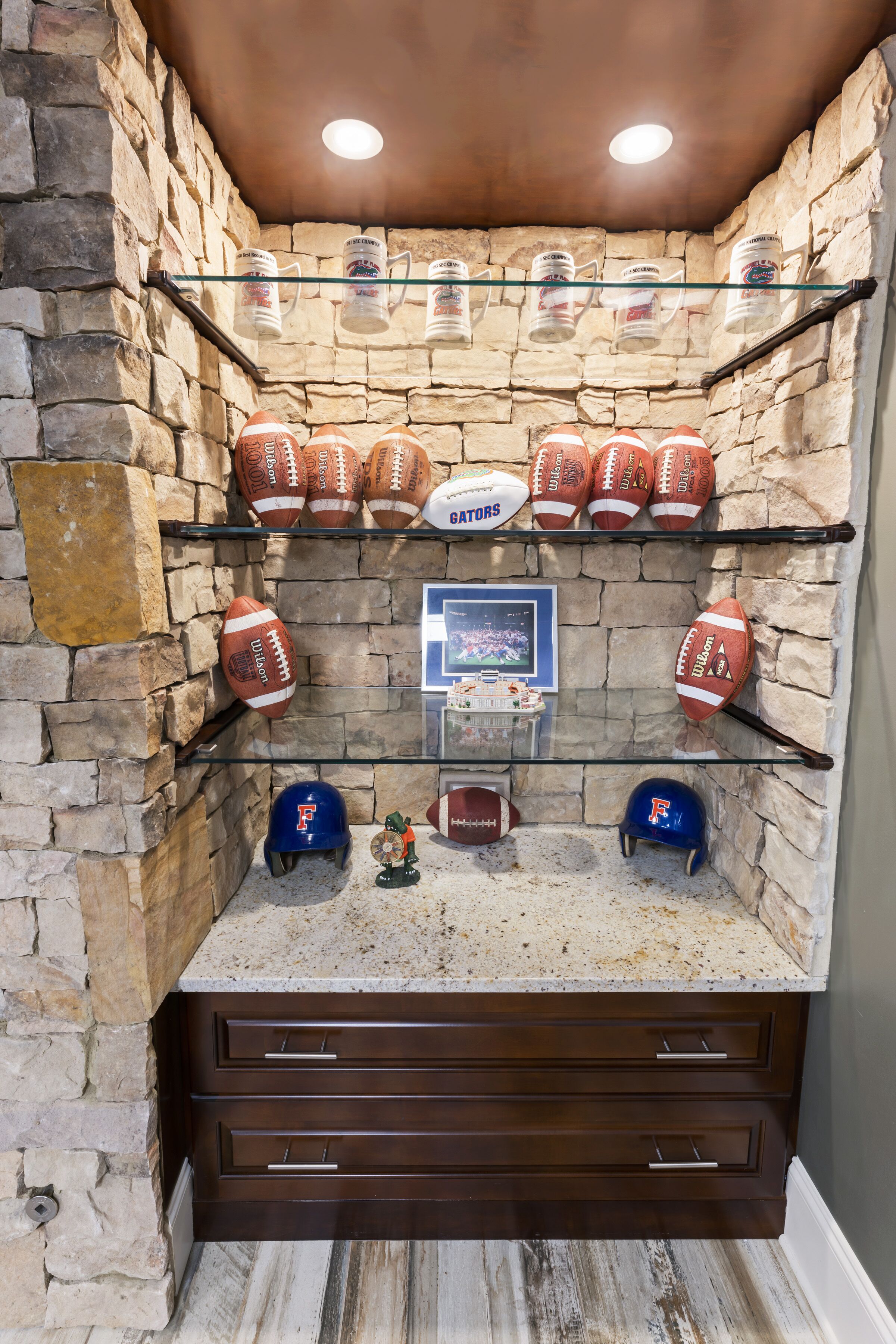 A stone-walled room with shelves displaying footballs and helmets, a framed picture, and a small figurine.