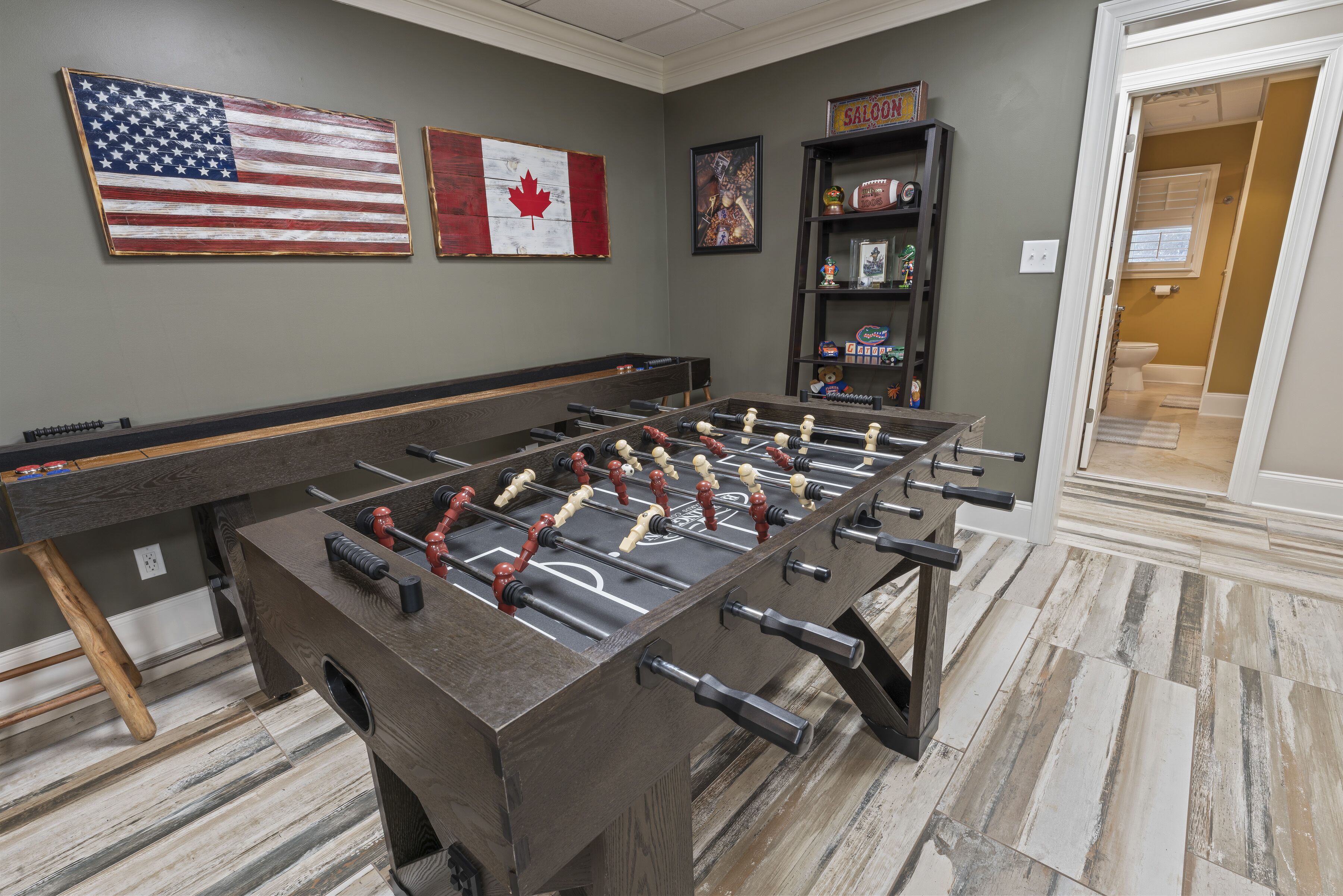 Uma mesa de futebolito numa sala com parede cinzenta, uma bandeira do Canadá e uma bandeira dos Estados Unidos.
