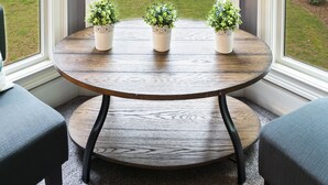 Habitación de esquina con un ventanal grande que da a un lago y árboles. Hay una mesa redonda de madera con dos plantas en macetas.