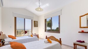 Une chambre d’hôtel avec deux lits, une petite table, une chaise, une lampe et une vue sur la mer.