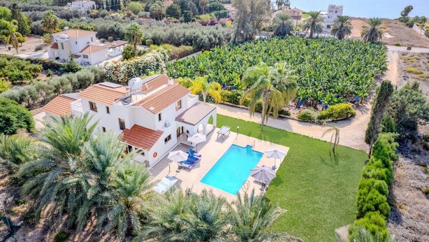 Une grande maison avec une piscine, entourée d’une végétation luxuriante et offrant une vue sur la mer.