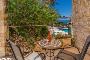 Une terrasse avec une table, des chaises et une bouteille de vin, donnant sur une piscine et la mer.