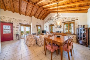 Un intérieur rustique avec des murs en pierre, des poutres en bois, un coin repas avec des motifs floraux sur les sièges et une cheminée en pierre.