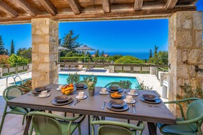 Zona pranzo all'aperto con tavolo apparecchiato per due, con vista su piscina e mare.