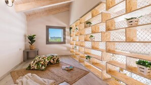 Una habitación acogedora con techo inclinado, una ventana con vistas, estantes de madera con plantas, un cojín estampado y una alfombra tejida.