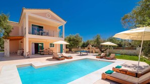 Ein zweistöckiges Haus mit Swimmingpool, Gartenmöbeln und Grillplatz.