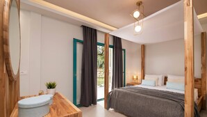 Ein modernes Schlafzimmer mit einem Holz-Waschtisch, einem großen Bett mit grauer Decke und Blick auf Grünfläche draußen.