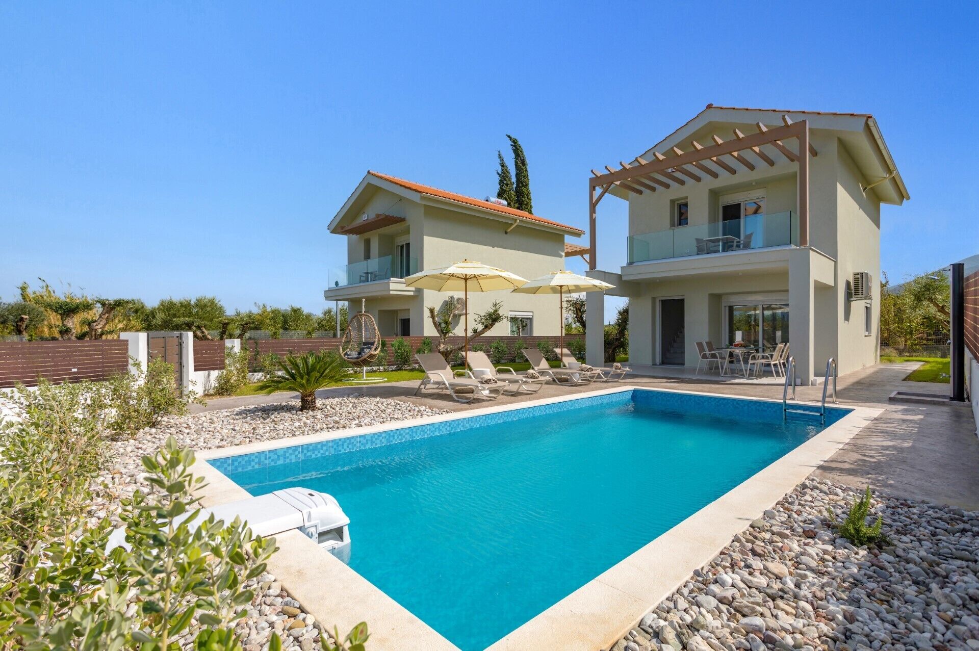 Una casa de dos pisos con piscina, mobiliario de exterior y una pérgola.