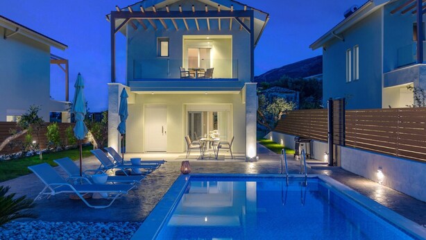 Una casa moderna de dos pisos amb una piscina, zona d'estar a l'exterior i un pati ben il·luminat.