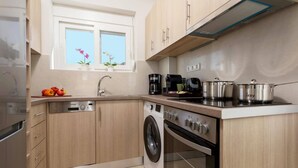 A compact kitchen with a washing machine, a coffee maker, and a stove. - Villa Vilenia Horizon by Villa Plus (Katastari)