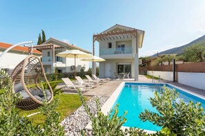 A modern two-story house with a swimming pool, outdoor seating, and a pergola.
