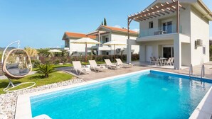 A poolside area with a clear blue pool, lounge chairs, and a hanging chair. - Villa Vilenia Horizon by Villa Plus (Katastari)