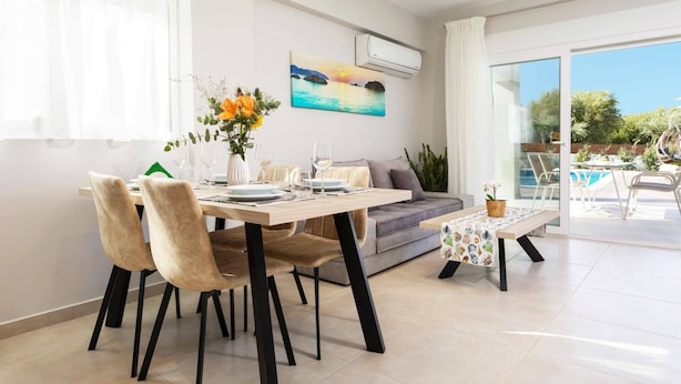 A dining area with a table set for two, a sofa, and a view of an outdoor pool. - Villa Vilenia Horizon by Villa Plus (Katastari)
