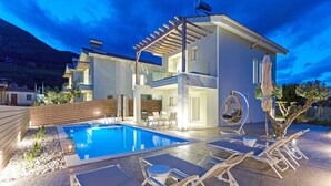 Una casa moderna de dos pisos con piscina, mobiliario exterior y un pérgola.