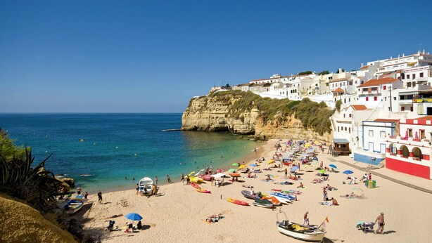 A beach with white buildings, clear blue water, and people sunbathing. - Villa Africa by Villa Plus (Praia do Carvoeiro)