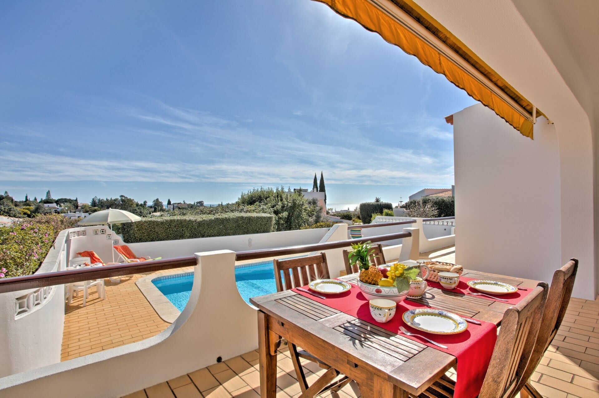 Une terrasse avec une piscine, une table à manger dressée avec des assiettes et des couverts, et une vue sur le paysage environnant.