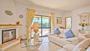 A living room with a fireplace, a glass coffee table, a sofa, and a view of the outdoors through a large window. - Villa Africa by Villa Plus (Praia do Carvoeiro)
