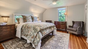Une chambre à coucher comprenant un lit, une table de chevet, une commode, une chaise et un ventilateur de plafond.