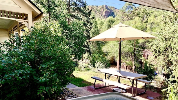 Un bain à remous avec une table et un parasol, entouré de verdure et offrant une vue sur la montagne.