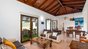A spacious living area with a wooden ceiling, a sofa, a coffee table, and a dining set.
