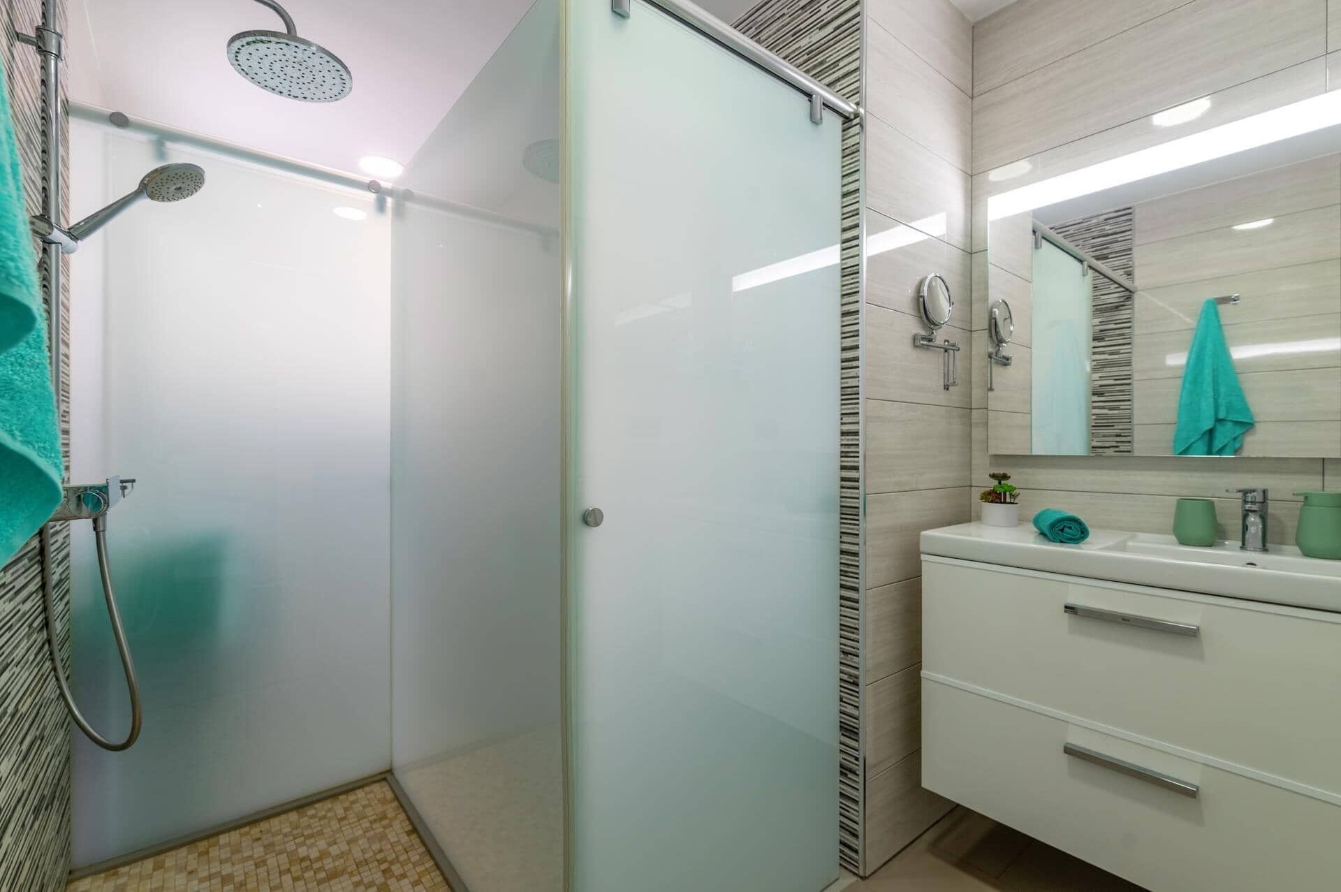 A modern bathroom with a glass shower enclosure, a white vanity with a mirror, and a tiled floor.