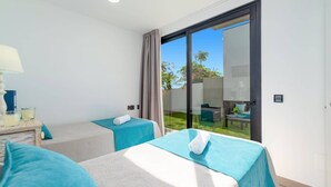 Hotelkamer met twee bedden, een nachtkastje, een lamp en uitzicht op een tuin door een schuifdeur.
