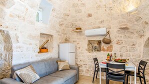 Ein gemütliches Zimmer mit Steinwand, einem grauen Sofa, einem Esstisch mit Stühlen und einer weißen Klimaanlage.