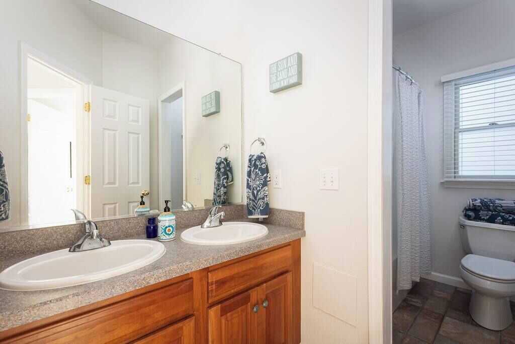 A bathroom with two sinks, a large mirror, wooden cabinets, and a toilet.