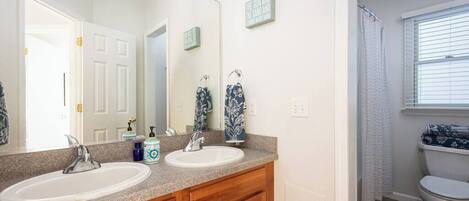 A bathroom with two sinks, a large mirror, wooden cabinets, and a toilet.