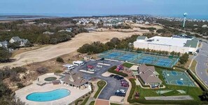 An aerial view of a residential area with a large building, a swimming pool, tennis courts, and a parking lot. - Sound Views, Pool, Hot Tub, Game Room, Club Access (Corolla)