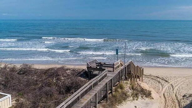 A wooden boardwalk leading to a beach with a clear view of the ocean.