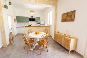 Une cuisine avec des meubles de couleur verte, un plan de travail blanc et un coin repas comprenant une table ronde et des chaises en bois.