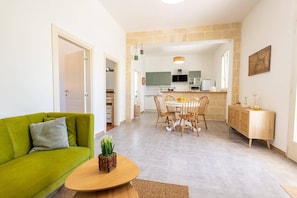Ein Wohnzimmer mit einem grĂŒnen Sofa, einem Holztisch und einem Essbereich mit Tisch und StĂŒhlen.