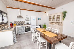 Eine kompakte KĂŒche mit weiĂen SchrĂ€nken, einem Esstisch mit StĂŒhlen und einem kleinen KĂŒhlschrank.
