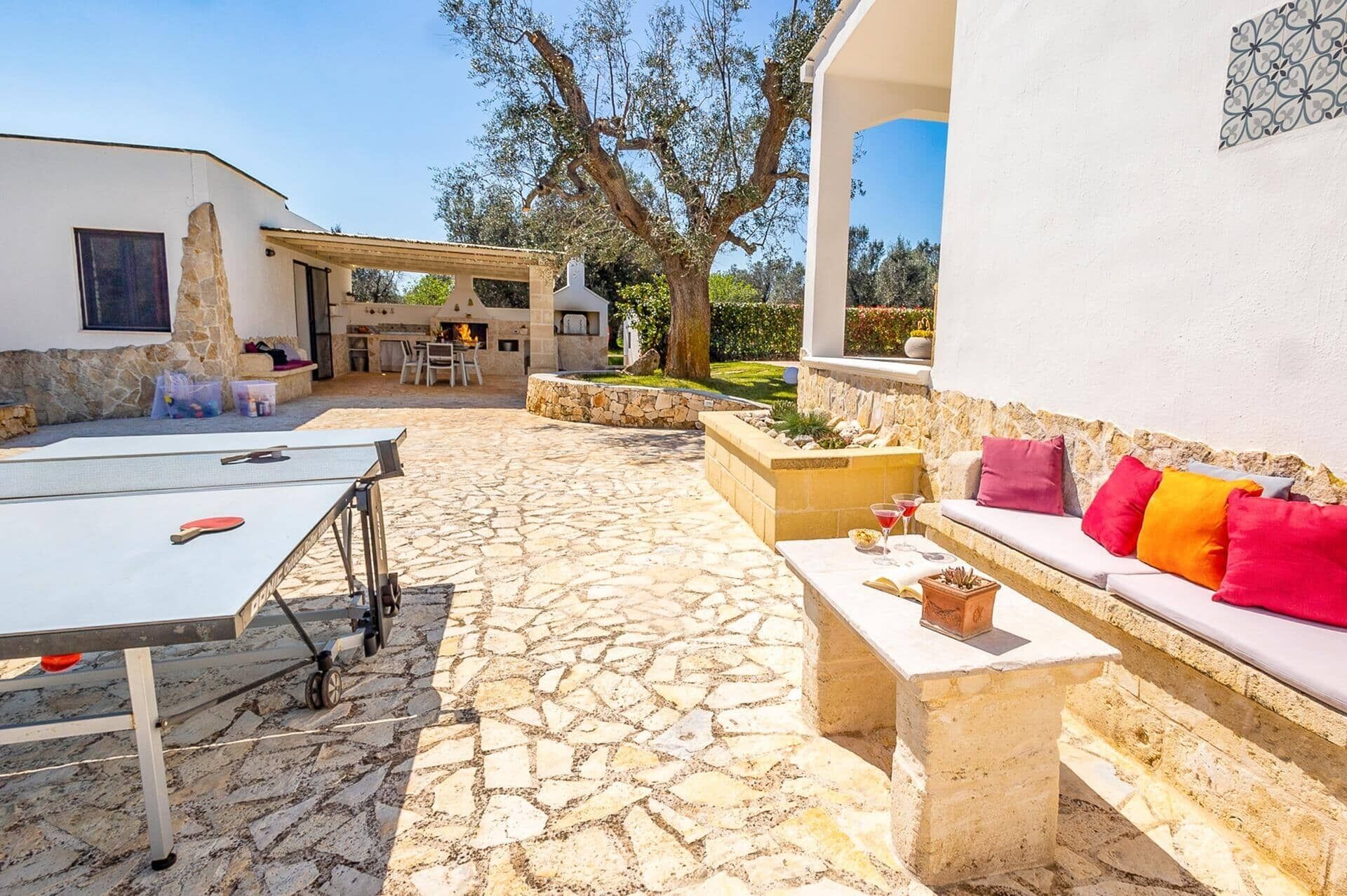 Un patio de piedra con mobiliario exterior, una zona de barbacoa y un muro de piedra.