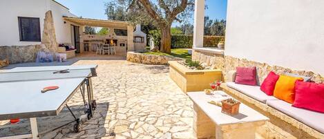 Un patio de piedra con mobiliario exterior, una zona de barbacoa y un muro de piedra.