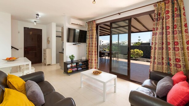 Ein Wohnzimmer mit Sofa, Couchtisch, Fernseher und einer Schiebetür zu einem Balkon.