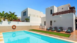 Ein moderner Poolbereich mit einem klaren, blauen Pool, Liegestühlen und einem weißen Gebäude mit Balkon.