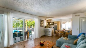 A spacious living area with a dining table, a sofa, and a kitchen in the background. - Villa Alpha by Villa Plus (Hersonissos)