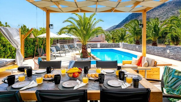 A dining area with a pool view, outdoor seating, and a mountain backdrop. - Villa Alpha by Villa Plus (Hersonissos)