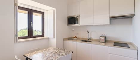 Cozinha compacta com armários brancos, micro-ondas, pia e mesa com cadeiras.