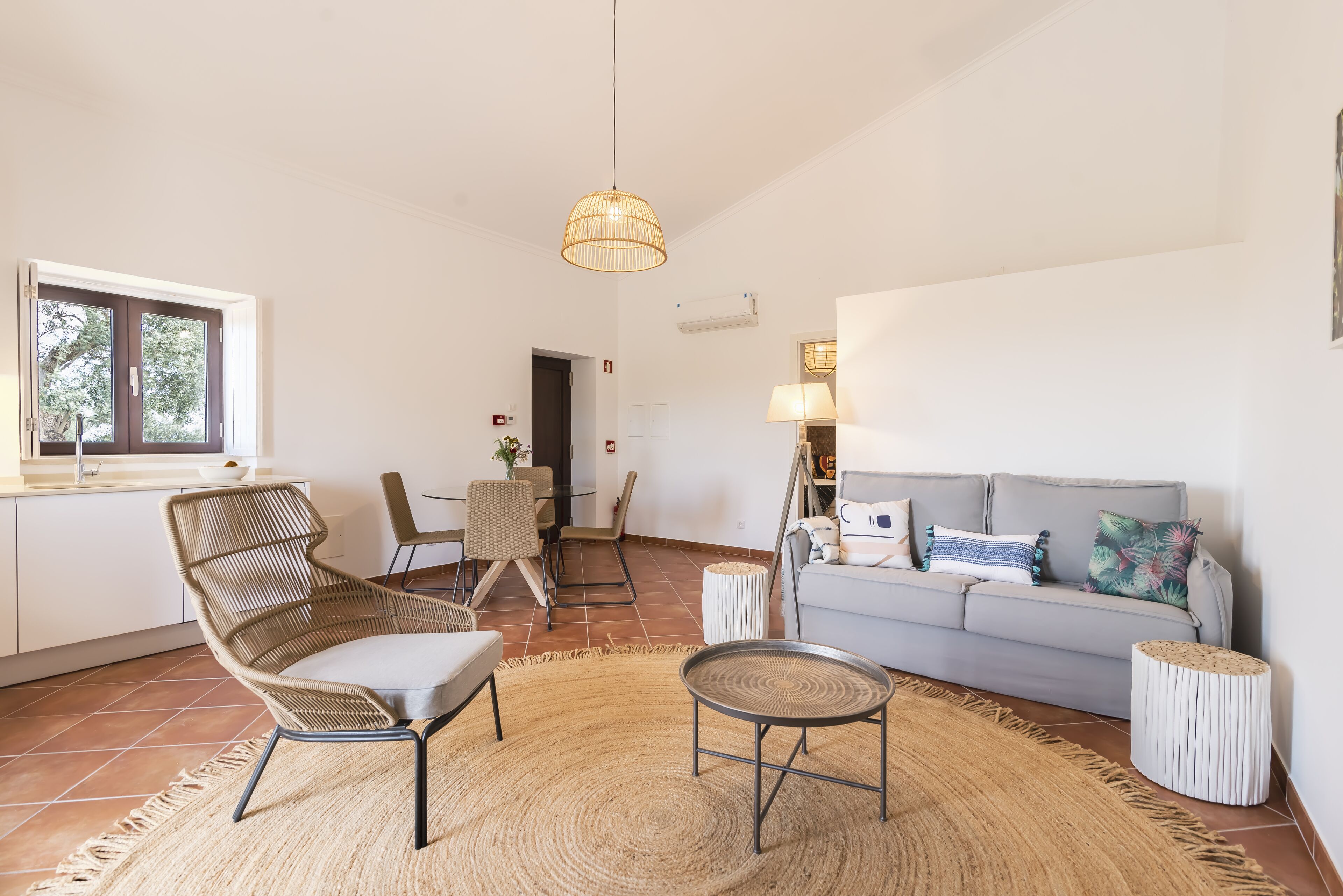 Een moderne woonkamer met een bank, een rieten fauteuil, een ronde salontafel en een hanglamp.