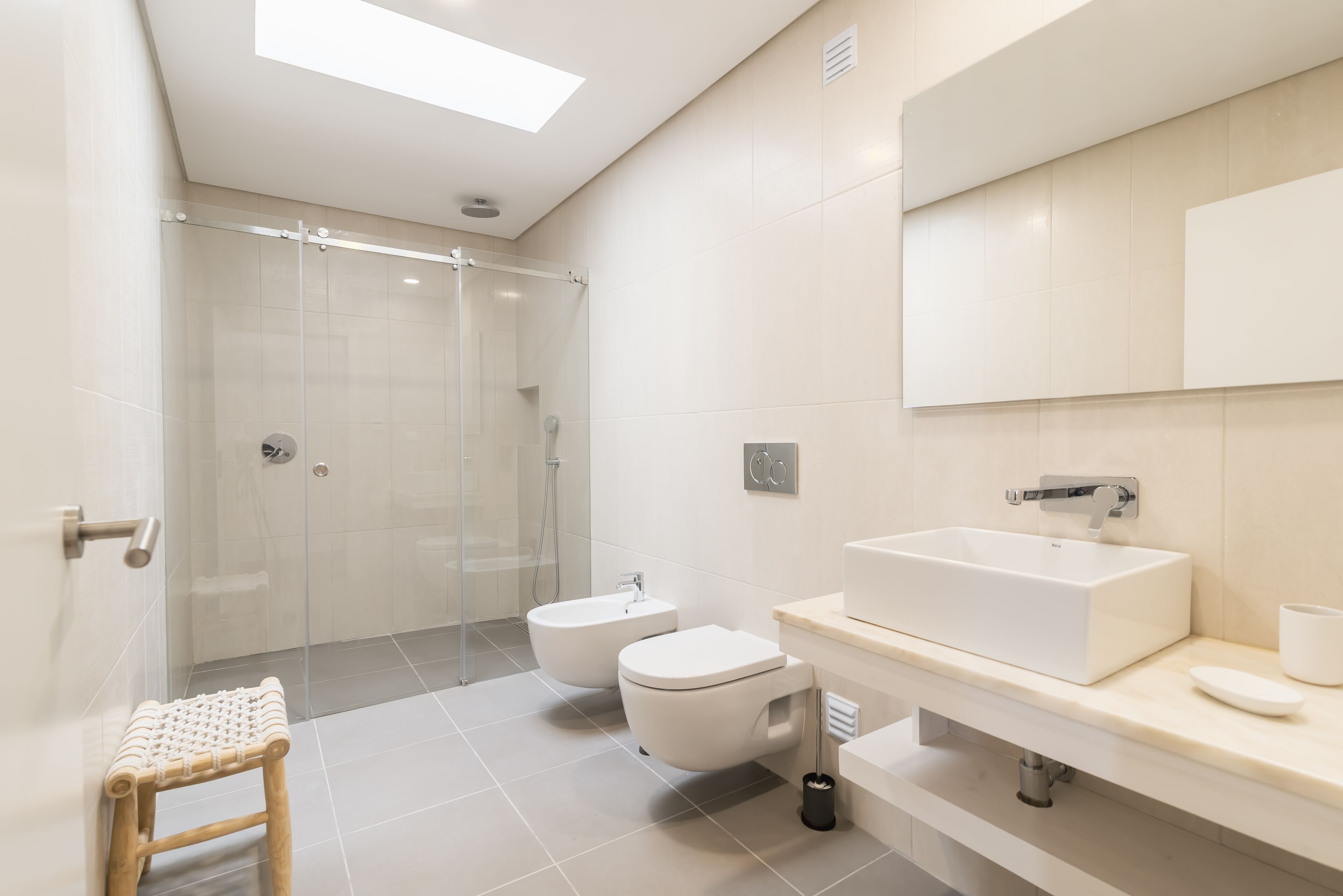 Een moderne badkamer met een douchecabine van glas, een bidet, een toilet en een grote wastafel met een spiegel erboven.