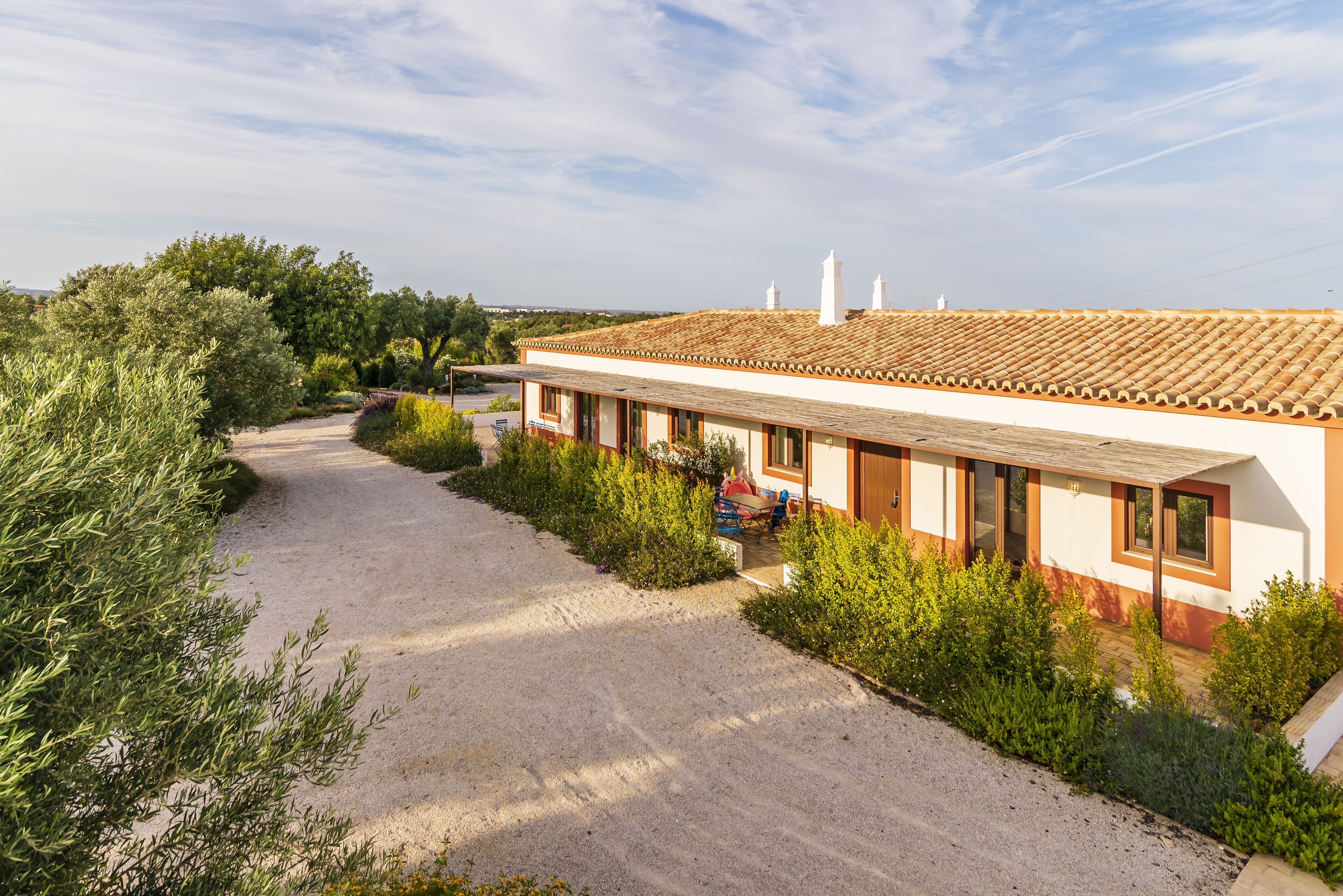 A building with a tiled roof, a gravel driveway, and surrounding greenery.
