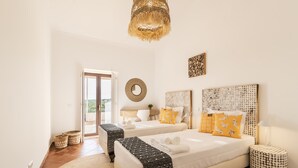 A bedroom with two beds, a woven headboard, a round wall decoration, and a view through a glass door. - Quinta da Baleeira (Tavira)