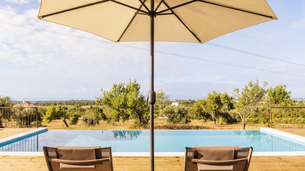 A poolside area with a wooden deck, two lounge chairs, a table, and an umbrella. - Quinta da Baleeira (Tavira)